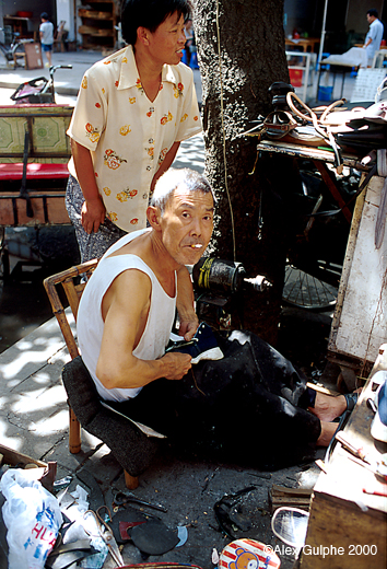 Photographie Couleur - Verticale - Cordonnier travaillant assis dans la rue sur une chaise en bambou