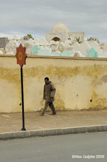 Photographie Couleur - Verticale - Homme avec un parapluie passant le long du mur d’un cimetière