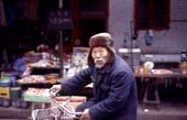 Photographie - Vieil homme à bicyclette devant un bazar