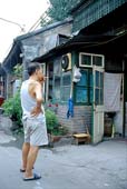 Photographie - Homme fumant devant une maison dans un quartier de hutong